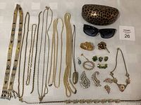 Full overview of jewelry assortment with necklaces, brooches, earrings, sunglasses, and Guess sunglass case on white cloth.