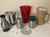 Image showing the entire lot including red glass vase, beige Tupperware pitcher, Stanley Thermos, nut chopper, canisters, and ashtray.