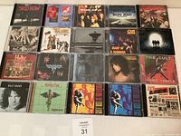 Top-down view of 22 classic rock music CDs laid out in 3 rows with clear cover art visible, featuring band logos and album artwork.