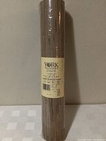 Single roll of York Wallcoverings grasscloth wallpaper wrapped in plastic with label showing brand and type.