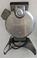 Closed view of the Cuisinart waffle maker showing stainless steel body, temperature dial, indicator lights, and power cord.