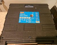 Closed view of the black plastic foldable Staples rolling crate, showing the top with handle recess and label sticker.