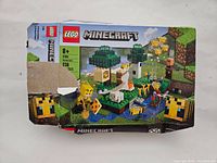 Photo showing front of Lego Minecraft set 21165 box with depiction of blocks, bees, and trees. The box has some damage.