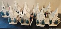 Nine porcelain village church LED musical decorations grouped together on a surface, showing identical style and trees with tags attached.