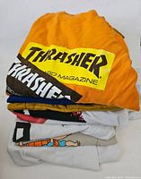 Stack of folded men's graphic shirts showing Thrasher, Supreme, and other designs