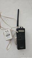 Radio Shack Pro-94 scanner laid flat with attached antenna and power adapter with cord shown beside it on a white surface.
