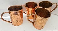Four copper mugs with hammered texture and handles, showing natural copper patina and some tarnish.