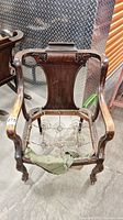 Front view of antique wooden chair without upholstery on seat, showing wood carving and caster wheels.