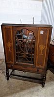 Front view of the antique china cabinet with glass door and wooden lattice design