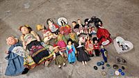 Full lot showing 12 vintage dolls in various costumes and a keepsake box with clip-on earrings and buttons.