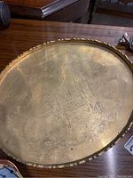 Close up photo of the brass tray showing etched design with people and nature scenes, the tray has a scalloped raised edge.