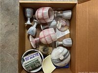 View of the box containing marble and stone goblets of different sizes and colors including a covered bowl with marbled pattern. One goblet has a broken stem.