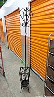 Full view of the metal coat rack with umbrella stand beside orange storage lockers. Tall structure with black metal frame and umbrella stand bottom.