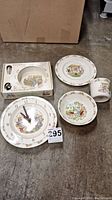 View of Royal Doulton Bunnykins child's dish set (plate, bowl, cup) and clock in box and out of box presenting the lot contents.