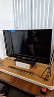 Full view of Samsung flat-screen TV on a wooden surface with stand and blue tape on corners.