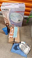 Photo showing the HoMedics Bubblemate foot spa in box, tanning kit components, and Philips travel iron coiled with power cord.
