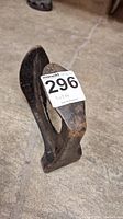 Front angled view of vintage cobbler's anvil tool with auction tag showing lot number 296, set on concrete floor.