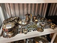 Full view of silver plated items including bell, bowl, cream and sugar, assorted trays and bowls