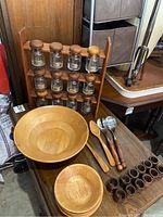 Full view of vintage teak spice rack with 12 glass jars, large salad bowl, smaller bowls, wooden utensils, and napkin holders on table.