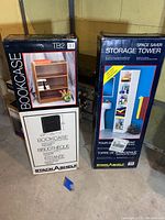 Two unopened boxed items: TB2 Bookcase and Space Saver Storage Tower in a basement storage setting.