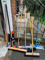Overall lot showing all items leaning against wall and stairs including brooms, mop and shovel.