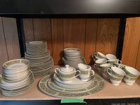 Full view of dinnerware set showing plates, bowls, mugs, saucers, platters, creamer, and sugar bowl arranged on shelf.