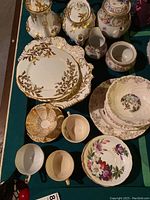Assorted plates, bowls, teapots, and cream and sugar sets arranged on a table. Features gold detailing and floral patterns evident on Johnson Bros and others.