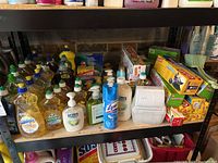 Shelf showing multiple bottles of dish soaps (Sunlight and Palmolive), liquid hand soap (Softsoap), Lysol disinfectant spray, hand sanitizer, and boxes of Glad trash bags.