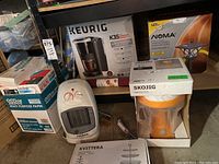 Photo showing boxed Keurig K35 coffee maker, Noma space heater, boxed Noma LED landscape lights, Kvittera serving dish box and instruction manual, and yellow silicon baking sheet in original packaging.