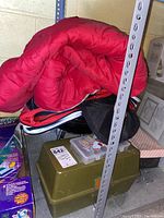 Red sleeping bag, black and red duffel bag, green fishing tackle box stacked in basement with other storage items