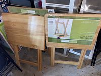 Two wooden folding tables shown stacked side by side with packaging label visible on one.