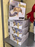 Seven boxed Galaxy Halogen Spot Light fixtures stacked on a metal shelf.