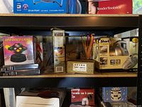 Assorted items on black shelving unit: UFO Disco Light, Corelle bake-and-serve dish, colored pencils and Shark Original vacuum