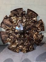 Front view showing entire round mirror with sculpted mythological and animal figures in a segmented gold-tone plastic frame