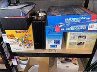 Image showing Soundesign Super 8 stereo in a sports-themed box, black briefcase, and two blue orthopedic seat cushion boxes labeled 'Seat Solution'.