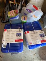 Two sealed packs of Mainstays brand plastic storage containers with blue lids, each containing multiple 12.9 quart size containers with gray buckle closures.