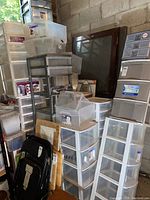 Several stacks of plastic drawer towers and bins against a cinderblock wall