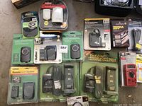Multiple new household items including outdoor mechanical timers, remote control systems, adhesive mounts, and Velcro strips arranged on a floor surface.