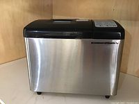 Front view of the stainless steel bread maker with black top and control panel on the side.