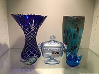 Front view of the collection showing the cobalt blue cut glass vase, mottled glass vase, clear lidded candy dish, and blue glass bird figurines