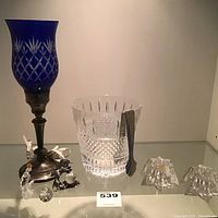 Photo showing blue cut glass lamp shade on silver plated lamp, lead crystal ice bucket with silver tongs, and two small cut glass figurines.