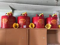 Four red steel safety cans with yellow spout caps and matching yellow funnels attached.