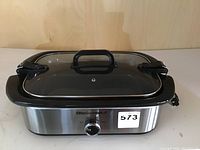 Full view of stainless steel slow cooker with locking transparent lid and black handle.