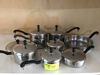Set of seven Faberware pots and pans including lids, showing front view on shelf.