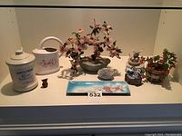 Photo showing entire lot with various ceramic containers, plastic plants, and figurines arranged on white shelf.