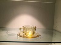 Cup with saucer in yellow Madrid depression glass under light on shelf.