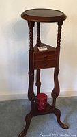 Side view of the mahogany plant stand showing barley twist legs, round top, two drawers, and the lower shelf candle holder with a red candle.