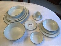 Full set arranged on table showing plates, bowls, cups and saucers with white-on-white floral embossed design and gold trim