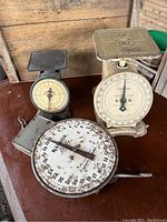Photo of all three antique scales: the Heaton milk scale with large circular dial, the black Preston postal scale with round dial, and the cream Universal household scale with square platform.