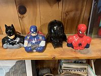 Front view of all four ceramic action figure banks in a row on a wooden shelf.